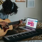 A person sitting on a bed playing guitar and keyboard